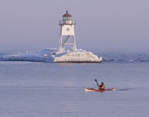 Kayaker paddling past the Grand Marais lighthouse in winter.